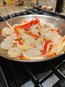 Raw shrimp and peppers being cooked in a pan