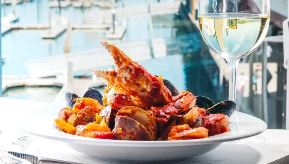 A Cioppino dish and a glass of white wine with the San Francisco Bay in the background.